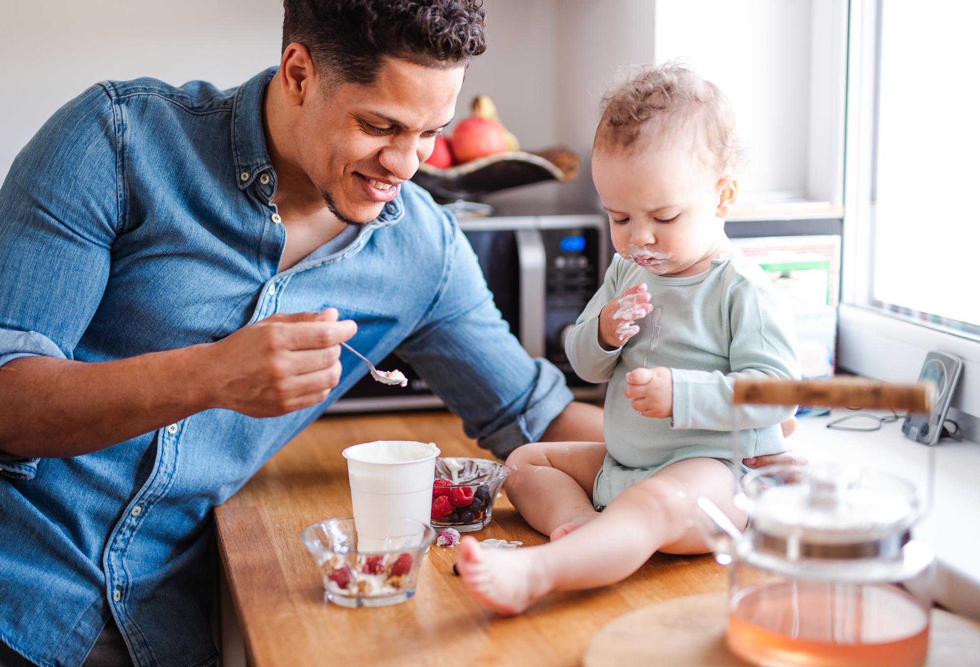 A father and a small toddler son eating fruit and yoghurt indoors at home