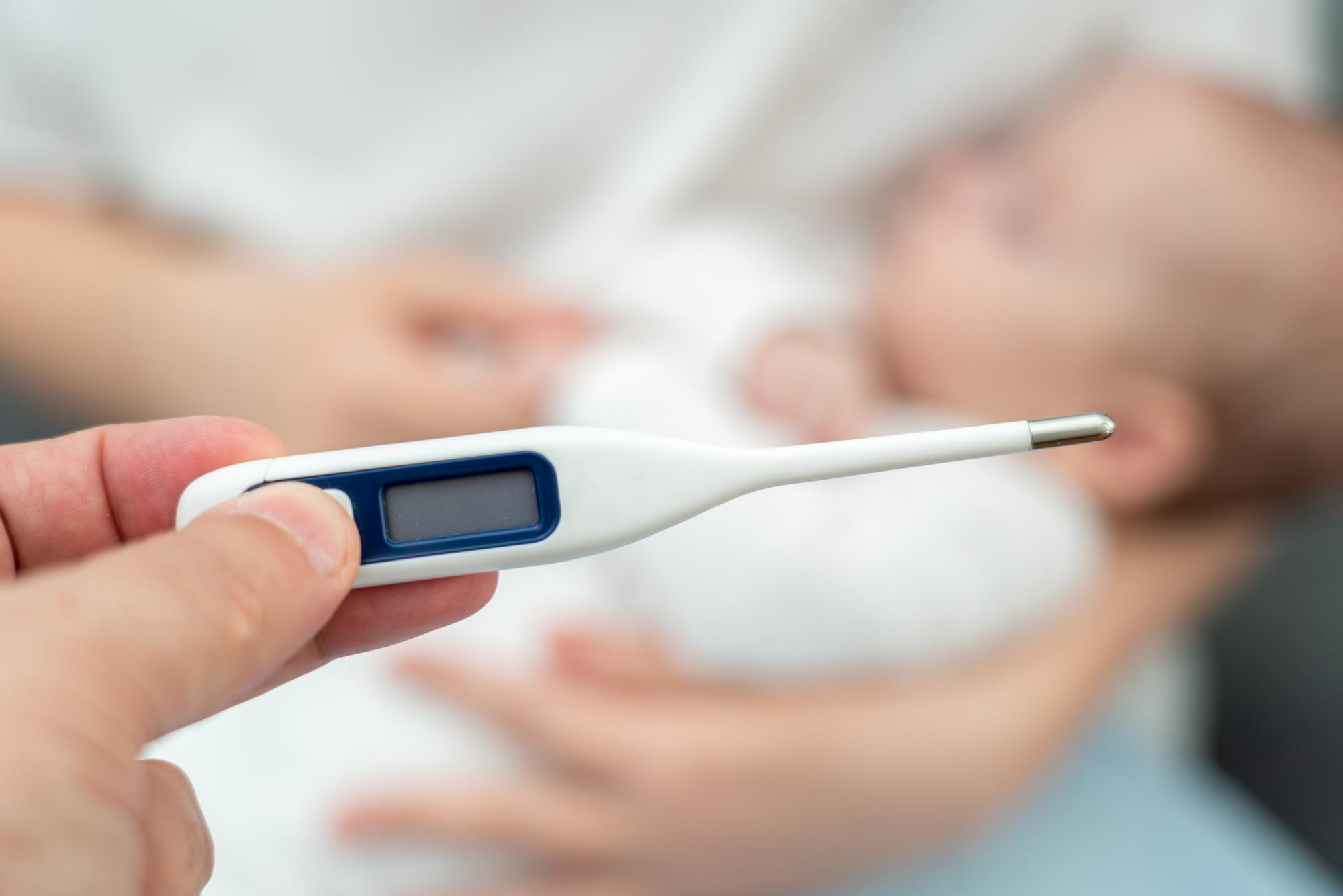 Parent checking newborn baby temperature with digital thermometer