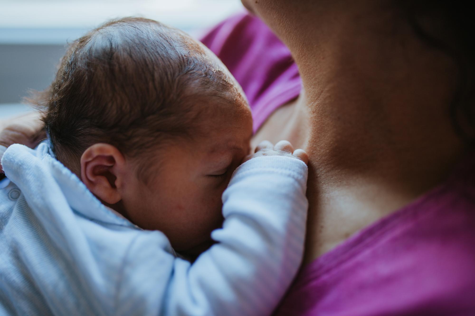 Newborn baby attempting to breastfeed with mother providing gentle support