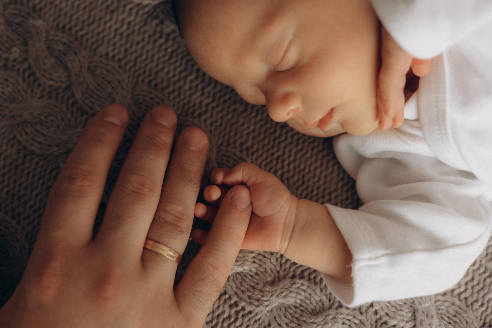 Peaceful newborn baby being gently comforted by parent hands in soft natural lighting